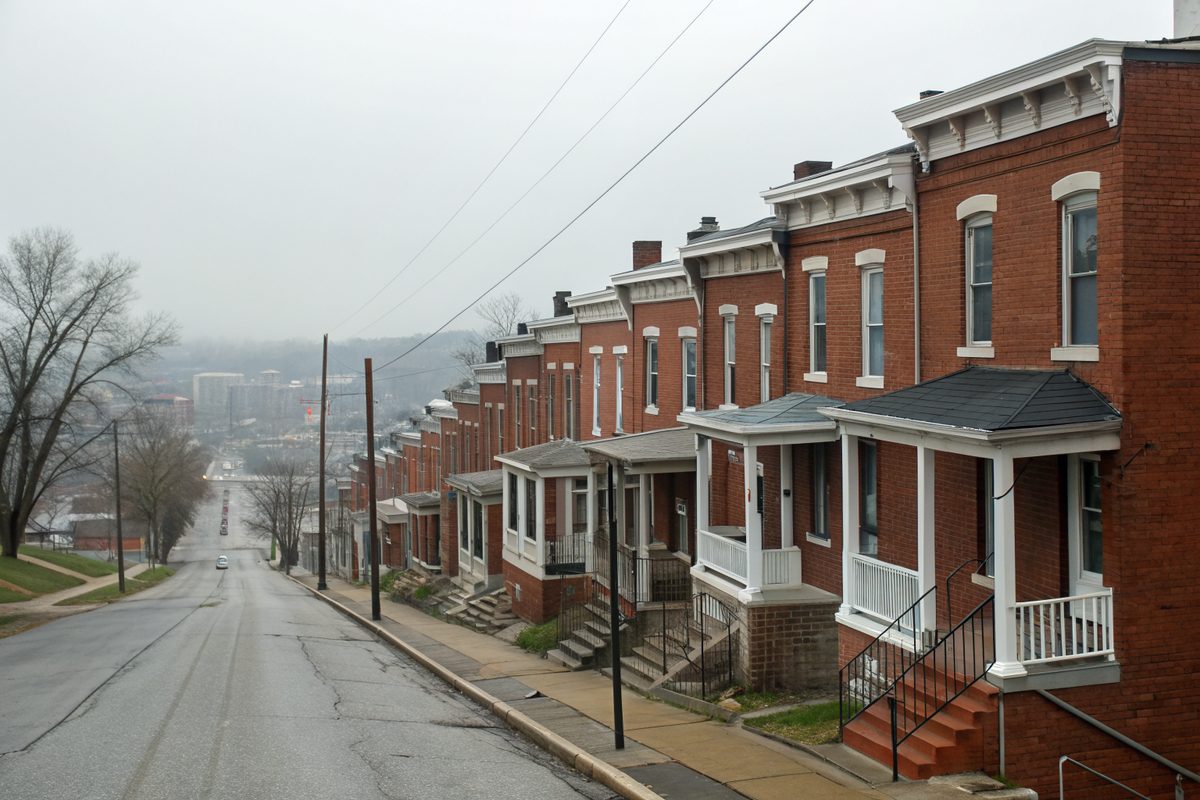 A row of attached brick row houses with flat roofs and cornices along a sloping street