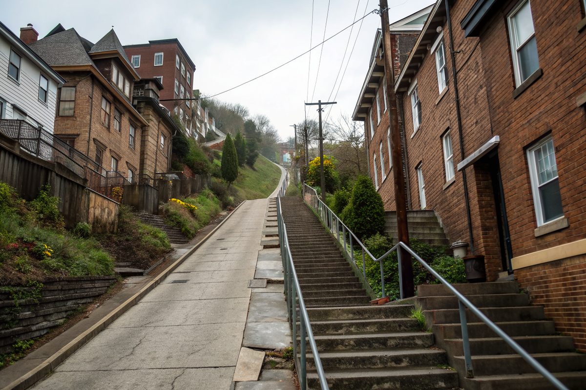 A steep street of older brick and frame houses with long public stairs climbing the hill