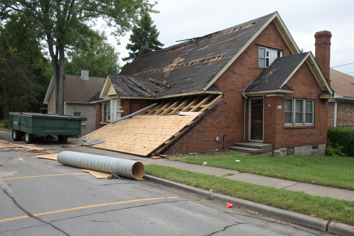 A brick house with part of its steep roof stripped to the decking and a dumpster at the curb